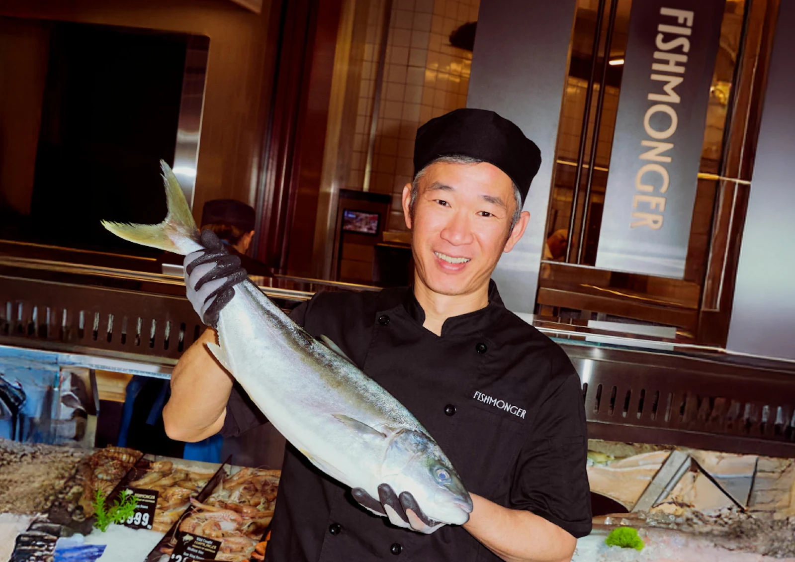 A chef holding a whole fish beside the vertical Fishmonger sign