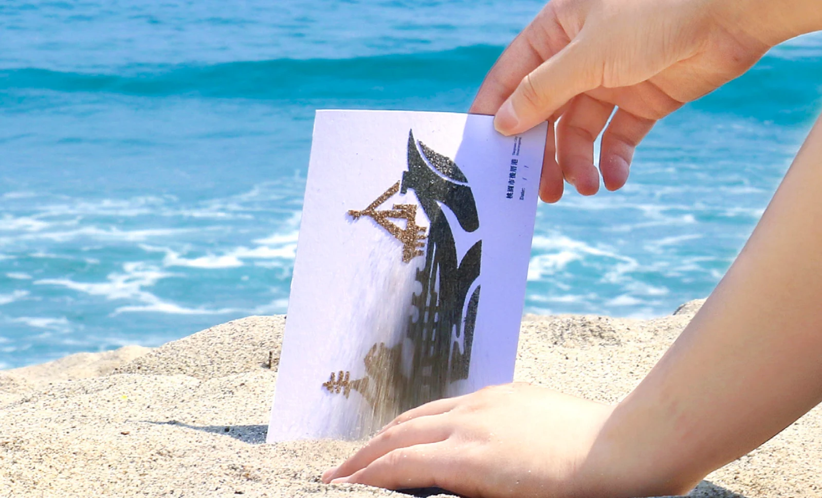 A postcard held against the sea and sand